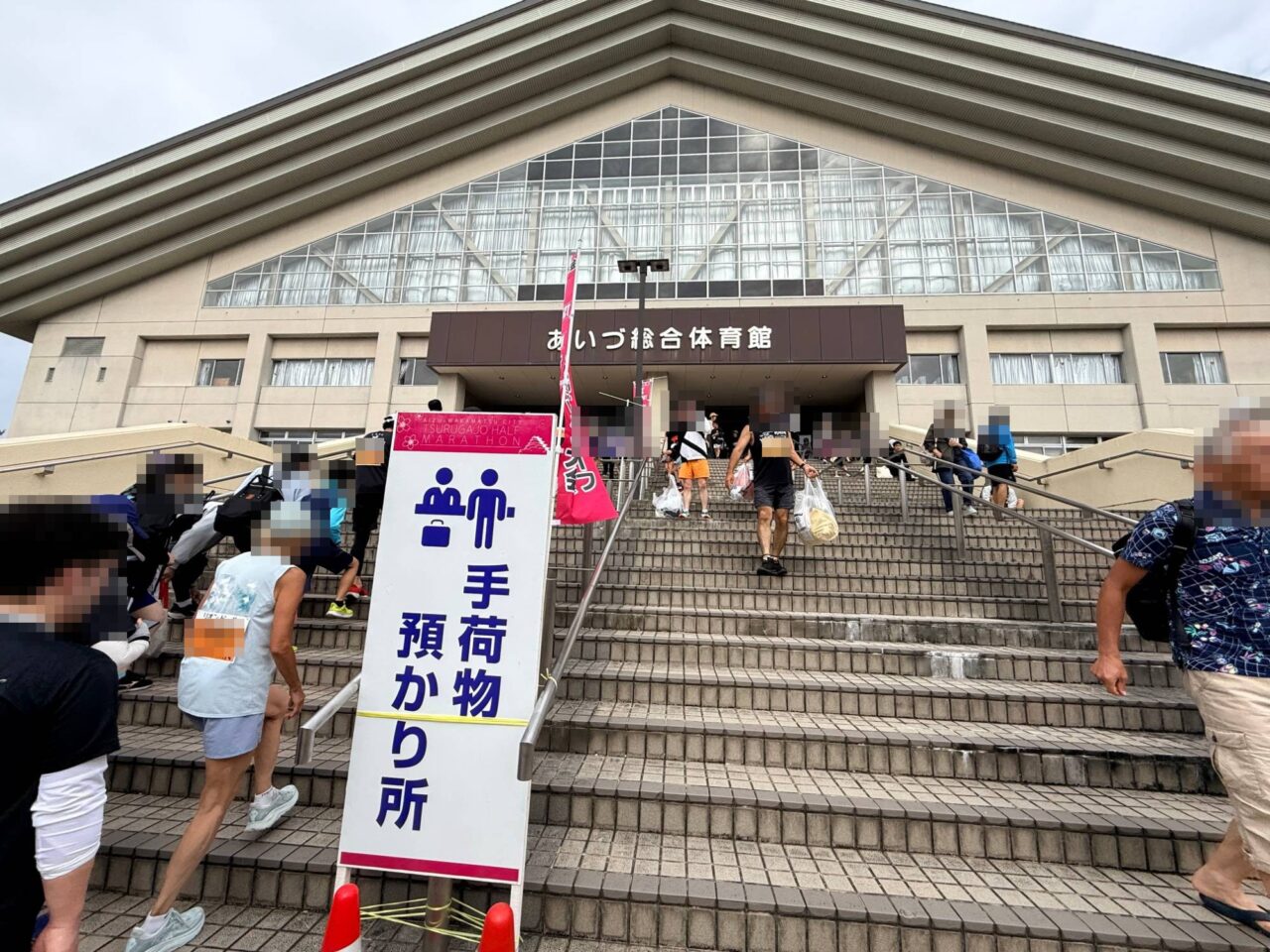 手荷物預かり所の看板が立つあいづ総合体育館の正面階段と行き交うランナー