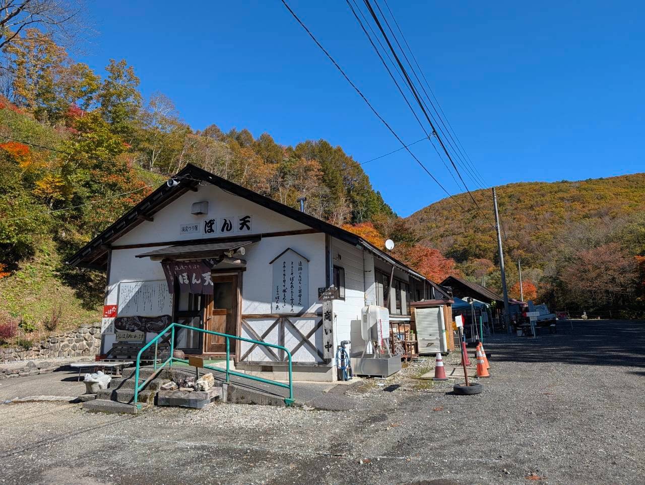 紅葉に囲まれた渓流つり堀ぼん天の白い外観と砂利の駐車場