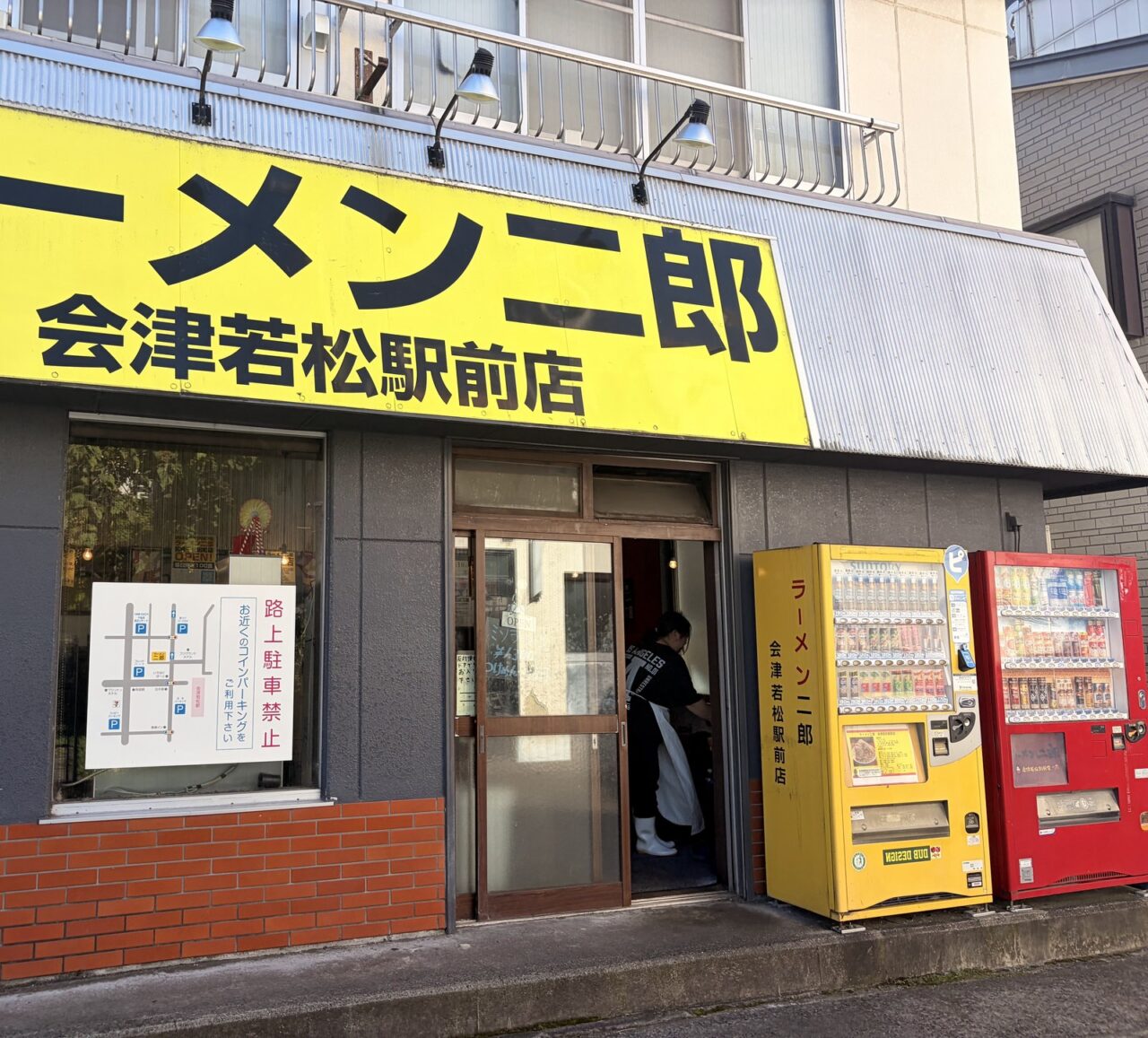 黄色い看板が掛かるラーメン二郎会津若松駅前店の外観と店頭の自動販売機