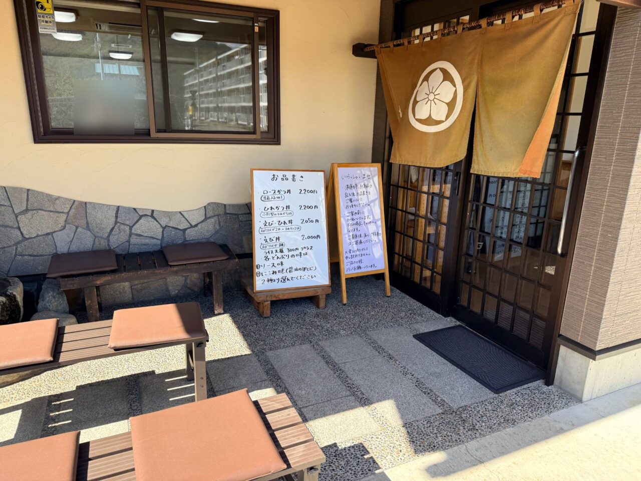 桔梗紋ののれんが掛かるお食事処むらいの入口と待合用のベンチ