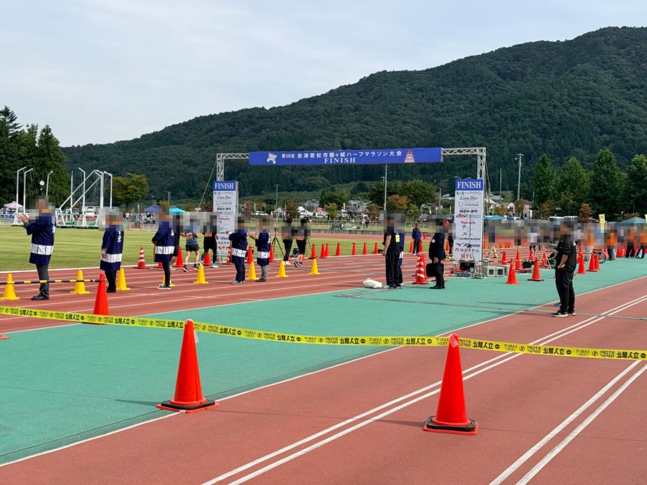 陸上競技場のトラックに設けられたFINISHゲートと、拍手で迎える法被姿の大会関係者